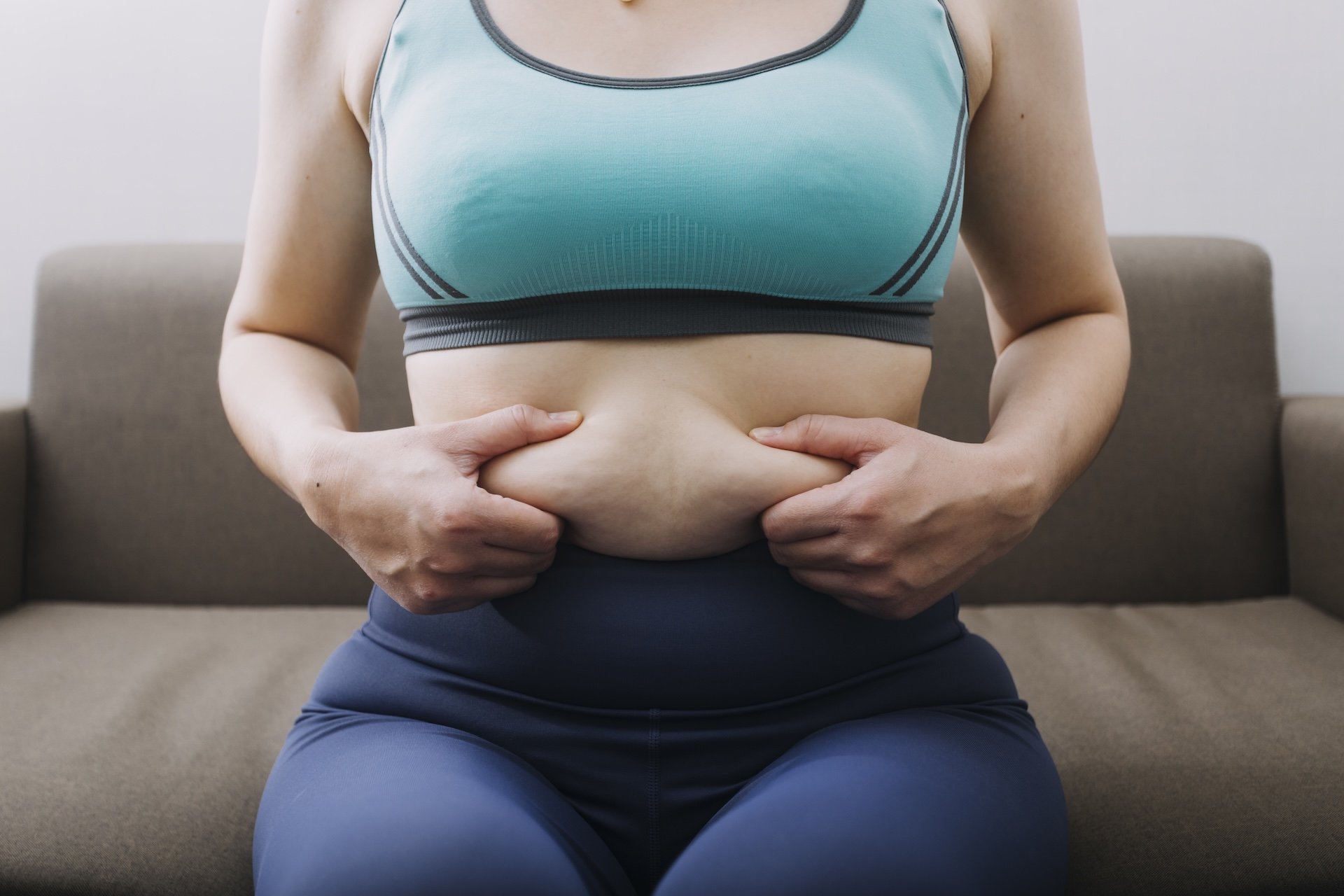 Woman measuring stubborn belly fat with a tape measure